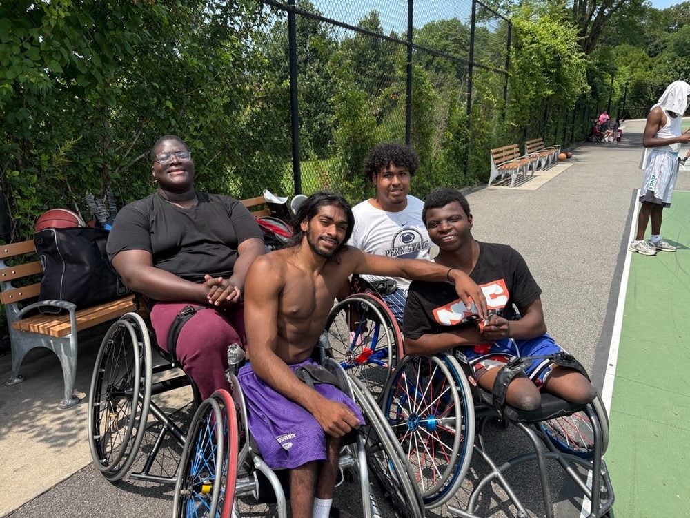Four Rolling Fury teammates in sport chairs smiling together on an outdoor court