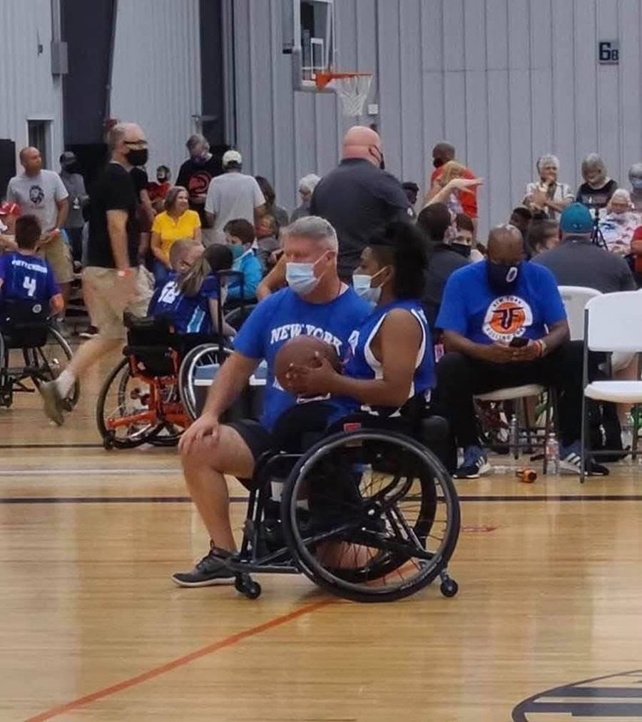 A Rolling Fury coach and player sharing a sport chair on the court during a game, teammates and family in the background