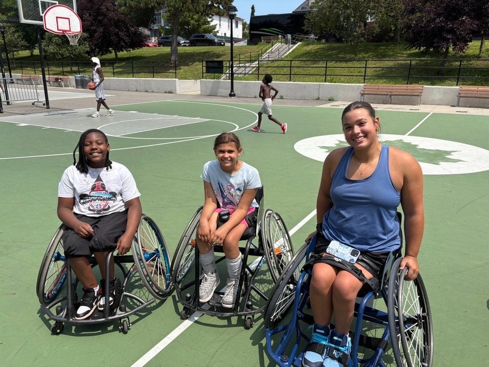 Three young Rolling Fury athletes in wheelchairs smiling together on an outdoor basketball court